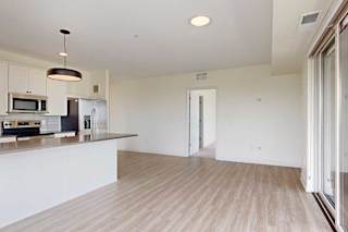 Modern open-concept kitchen and living area with light wood flooring, stainless steel appliances, and natural light streaming in.