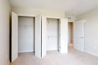 Empty room with light beige walls and carpet, a closet with two open white double-door with shelving.