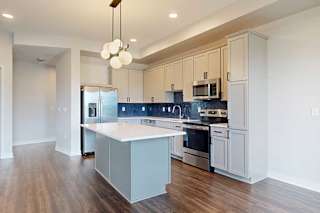 Modern kitchen with white cabinets and a blue backsplash, featuring stainless steel appliances