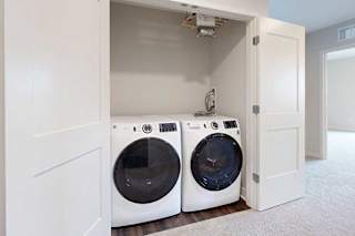 Two white front loading washing machines in a closet with double doors