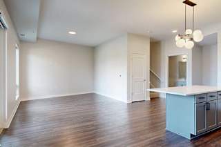 Modern kitchen and living area in neutral tones. Wood flooring, white walls, pendant light fixture, and open island countertop create a spacious feel.