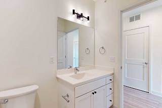 Modern bathroom with a clean, minimalist design. Features a large mirror, white vanity, sink, and a toilet.