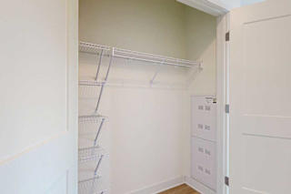 Small, empty closet with white wire shelves on left and top walls, cream-colored walls, wooden floor, and open white door;