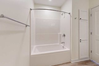 Simple bathroom with a white bathtub-shower combo, curved shower rod, and beige walls. Wooden floor, towel bar, and a cabinet beside a door.
