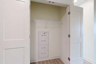 A white door is open to a hall closet with a white wall and a white shelf.