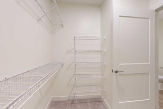 Empty walk-in closet with beige walls and white wire shelving on the left and back walls. A partially open white door is visible