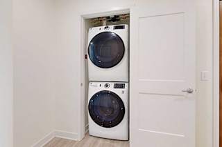 Stacked washer and dryer in a small closet with an open white door, placed on light wooden flooring.