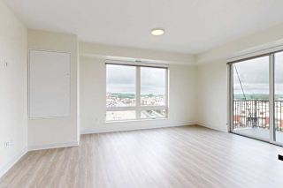 A bright, unfurnished apartment room with light wood floors, large windows showing a cloudy sky and cityscape, and a small balcony, conveying spaciousness.
