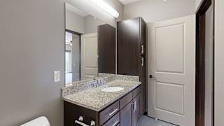 a bathroom vanity with large mirror, light granite countertops, and dark cabinets