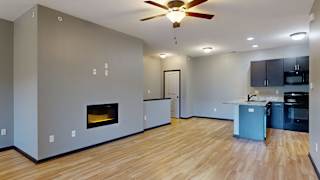 an empty living room with a fireplace and kitchen in the background