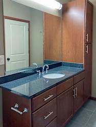 A bathroom with a wide granite vanity sink, tall storage cabinet, and large mirror.