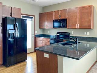 A kitchen with wooden cabinets, dark granite countertops, black appliances, and a door to a balcony.