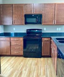 A kitchen with wooden cabinets, dark granite countertops, and black appliances.