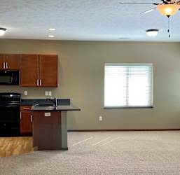 A kitchen with a peninsula countertop that opens to a spacious living room with large windows.