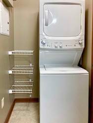A stacked full-size washer and dryer in a laundry room with built-in shelves.