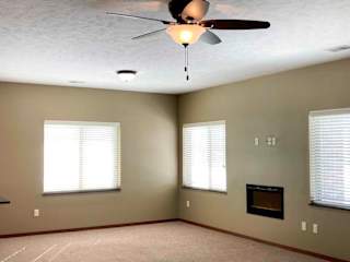A living room with several large windows, an electric fireplace, and a ceiling fan.
