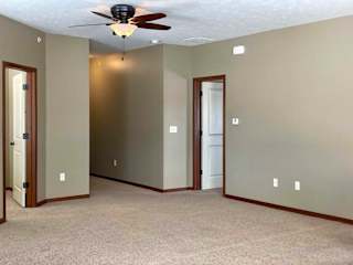 A living room with a ceiling fan and doors to the bedroom and den space.