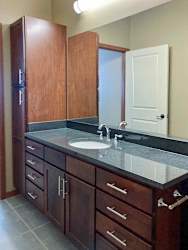 A long bathroom with a wide granite vanity sink, oversized mirror, and tall storage cabinet.