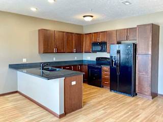 A kitchen with granite countertops, wooden cabinets, black appliances, and a peninsula counter.