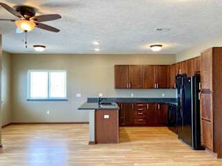 A kitchen with granite countertops, wooden cabinets, black appliances, and a peninsula counter next to a dining area with windows.