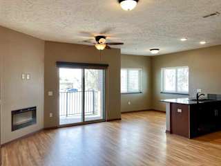 A living room with a ceiling fan, sliding glass door to a balcony, and electric fireplace.