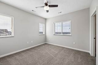 Spacious apartment bedroom with carpeted flooring, a ceiling fan, two windows with blinds providing natural light, and a sliding closet door.