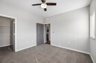 Spacious apartment bedroom with carpeted flooring, a ceiling fan, a walk-in closet, and a window with blinds providing natural light.