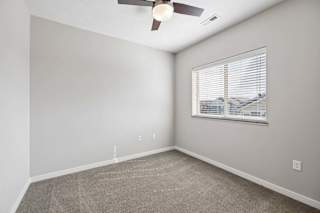 Bright apartment bedroom with carpeted flooring, a ceiling fan, neutral walls, and a window with blinds providing natural light.