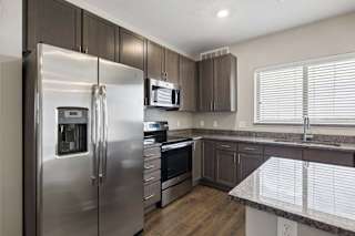 Modern apartment kitchen with dark cabinetry, granite-look countertops, stainless steel appliances, and a large window above the sink providing natural light.