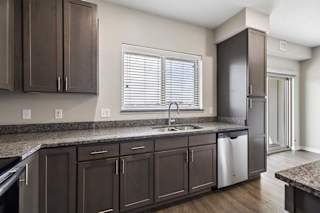 Modern apartment kitchen with dark cabinetry, granite-look countertops, a stainless steel dishwasher, and a large window above the sink providing natural light.