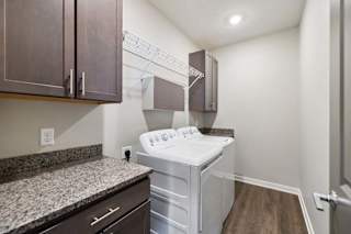 Apartment laundry room with side-by-side washer and dryer, granite-look countertop, dark cabinetry, built-in wire shelving, and wood-style flooring.