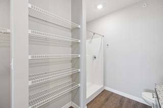 Apartment bathroom with built-in wire linen shelves, a tub-shower combination with a white surround, and a single-sink vanity with dark cabinetry.