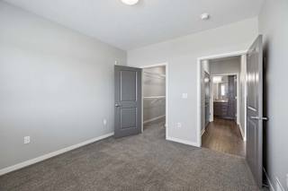 Bright apartment bedroom with carpeted flooring, an open closet with sliding doors, gray interior doors, and access to the adjoining hallway.