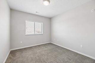 Bright apartment bedroom with carpeted flooring, neutral walls, and a window with blinds that provides natural light.