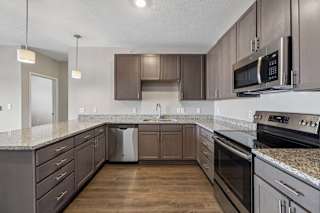 Modern apartment kitchen with dark cabinetry, granite-look countertops, stainless steel appliances, and a spacious U-shaped layout with ample counter space and storage.