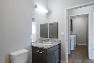 a bathroom with a sink and a mirror across a hallway from a laundry room