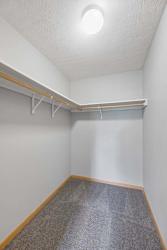 Spacious walk-in apartment closet with carpeted flooring, wraparound hanging rods, and built-in shelving.