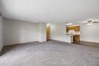 Expansive apartment living room with plush carpeting, an open breakfast bar, and a connected dining area and kitchen.