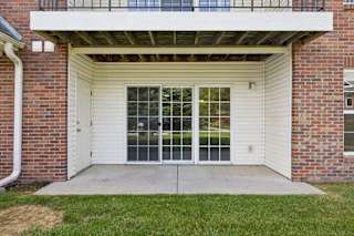 Covered ground-floor apartment patio with a concrete seating area, sliding glass door, and grassy lawn.