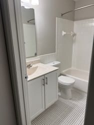 A white toilet sits in a bathroom next to a sink and a bathtub.