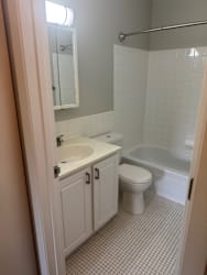 A white toilet is in a bathroom with a sink and tub.