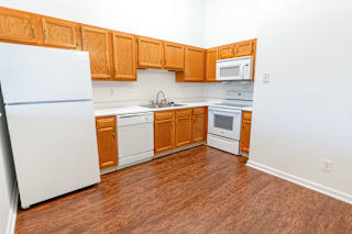 an empty kitchen with white appliances and wooden cabinets at Barton Farms in Greenwood, IN 46143