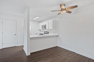 an empty living room with a ceiling fan and a kitchen