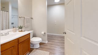 A white toilet sits in a bathroom with wooden floors and white walls.