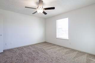 Empty bedroom in a model unit with a ceiling fan and natural light from a large window.