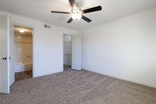 Empty bedroom in a model unit with a ceiling fan and natural light from a large window.