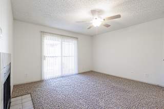 Spacious living room at Skyler Ridge featuring a fireplace, ceiling fan, and sliding door to a balcony.