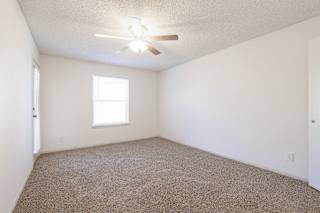 Empty bedroom in a model unit with a ceiling fan and natural light from a large window.