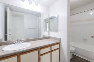 A bathroom in a model unit at Skyler Ridge Complex, featuring a sink, a shower, and a mirror.