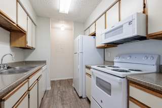 A kitchen in a model unit at Skyler Ridge Complex features white appliances, a sink, a refrigerator, and a stove.